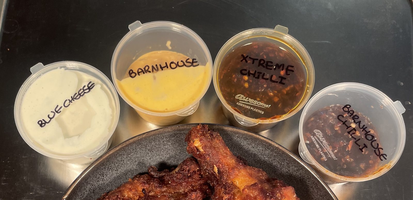 Four tubs of house sauce labelled by hand in black marker: blue cheese, Barnhouse, extreme chilli and Barnhouse chilli